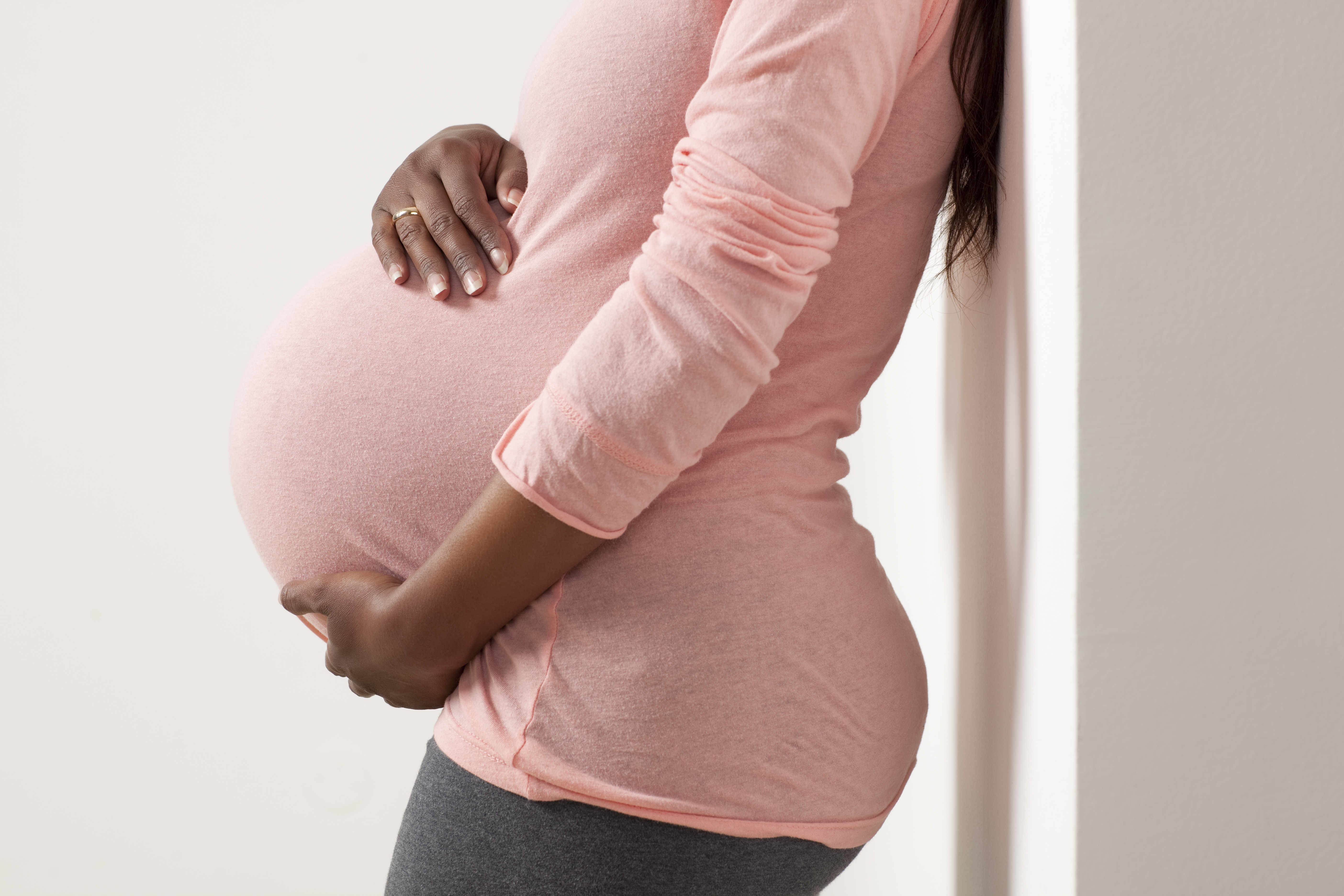 A pregnant woman in pink clothes having pain, holding her big belly.