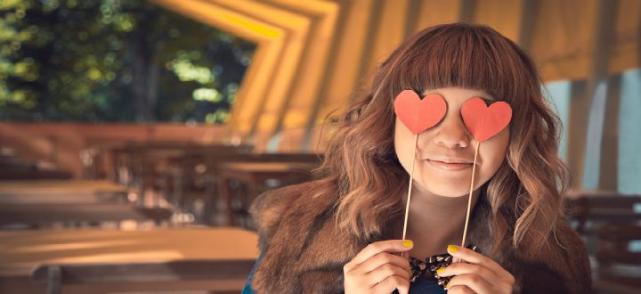 Teenage girl holding paper hearts over her eyes